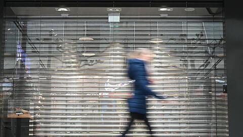 Eine Frau geht auf der Frankfurter Einkaufsmeile Zeil an einem Geschäft vorbei, an dem noch das Rollgitter heruntergelassen ist. Durch die Corona-Krise droht vielen innerstädtischen Geschäften das Aus.