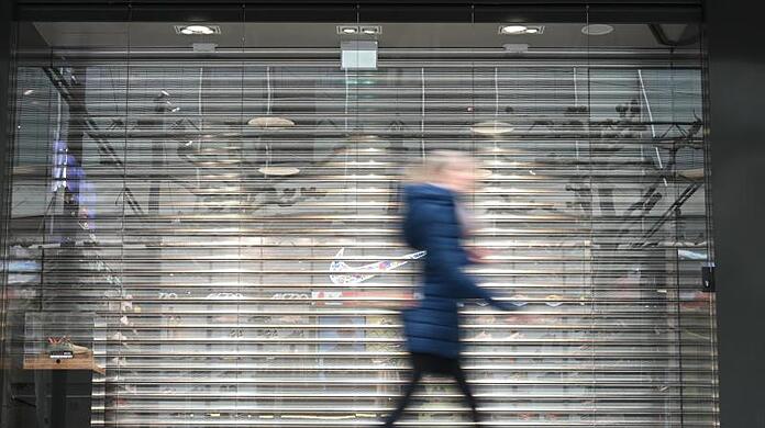 Eine Frau geht auf der Frankfurter Einkaufsmeile Zeil an einem Geschäft vorbei, an dem noch das Rollgitter heruntergelassen ist. Durch die Corona-Krise droht vielen innerstädtischen Geschäften das Aus.