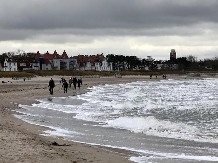 Spaziergänger sind bei stürmischem Wind an der aufgewühlten Ostsee in Warnemünde unterwegs.