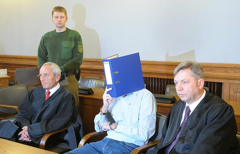 Der Angeklagte Guido N. (M) schützt sich zwischen seinen Anwälten Erhard Frank (l) und Malte Heise (r) mit einem Aktenordner vor dem Medieninteresse im Gerichtssaal des Landgerichts Leipzig.