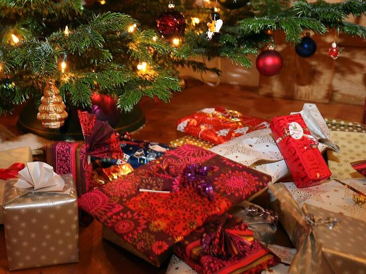 Verpackte Weihnachtsgeschenke liegen unter einem Christbaum.