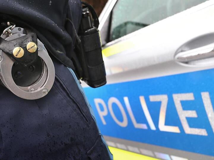 Ein Polizist mit Handschellen und einer Pistole am Gürtel steht vor einem Streifenwagen. Foto: Karl-Josef Hildenbrand/dpa/Symbolbild