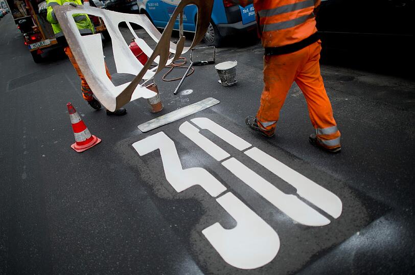Ab auf die Bremse! Zwei Arbeiter bringen das zeichen einer Tempo-30-Zone auf einer Straße an.