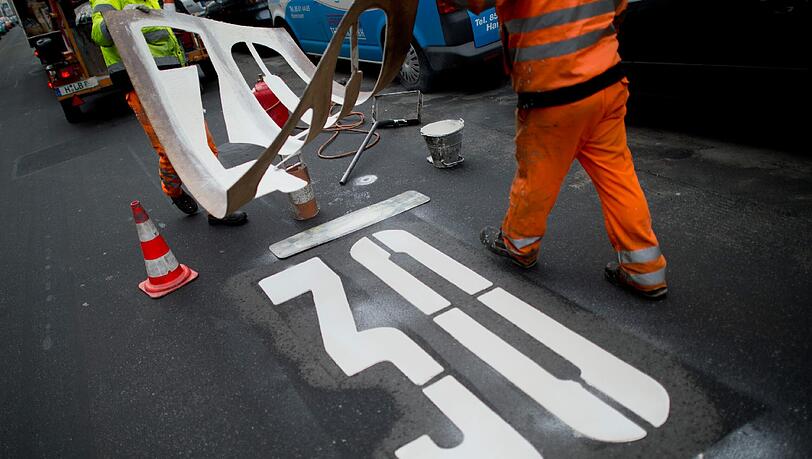 Ab auf die Bremse! Zwei Arbeiter bringen das zeichen einer Tempo-30-Zone auf einer Straße an. Ab auf die Bremse! Zwei Arbeiter bringen das zeichen einer Tempo-30-Zone auf einer Straße an.