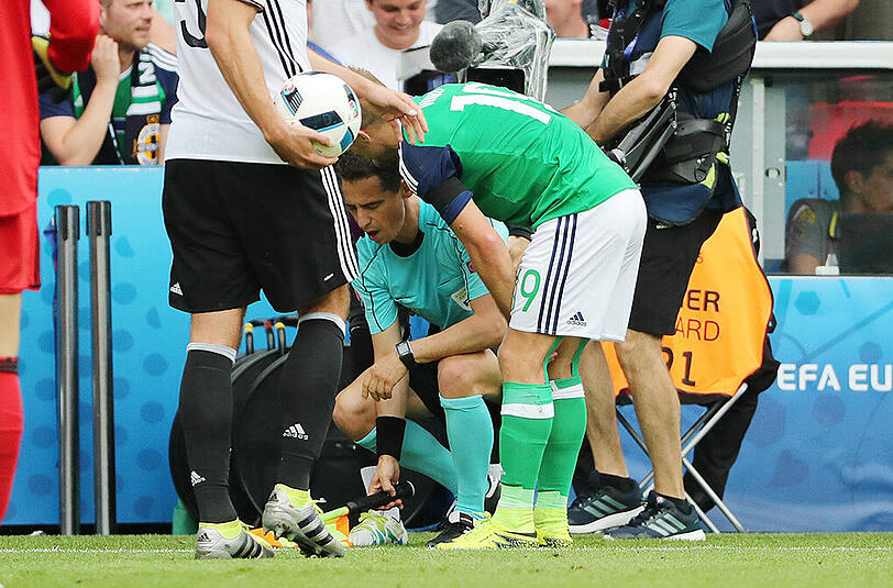 Bastian Schweinsteiger und Nordirlands Jamie Ward (rechts) helfen dem französischen Schiedsrichter-Assistenten Fréderic Cano (Mitte) auf die Beine.