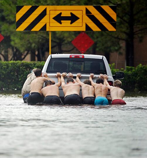 Sechs Männer schieben in Houston einen Kleintransporter über eine überflutete Straße.