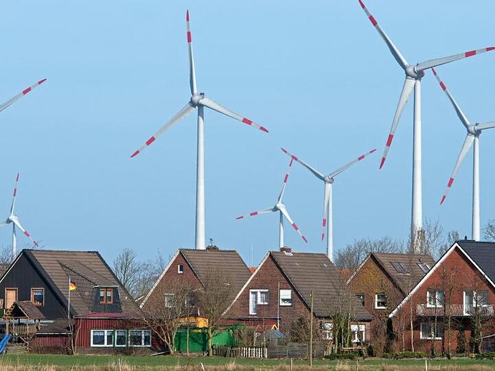 Windräder eines Windparks drehen sich dicht hinter einer Wohnsiedlung.