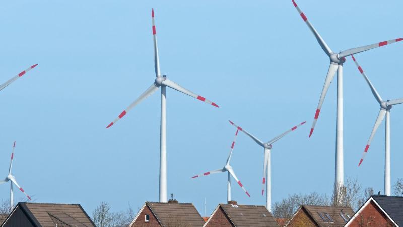 Windräder eines Windparks drehen sich dicht hinter einer Wohnsiedlung. Windräder eines Windparks drehen sich dicht hinter einer Wohnsiedlung.
