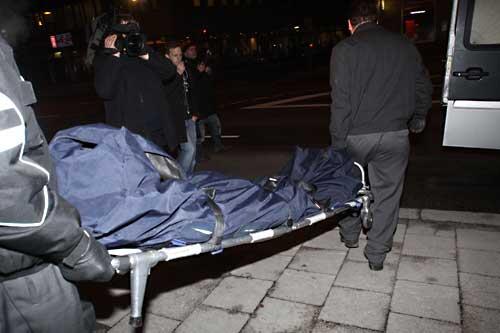Zwei Männer tragen die Leiche des Ermordeten auf einer Bahre aus dem Haus.