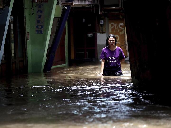 Eine Frau watet durch das Hochwasser einer überschwemmten Straße in Jakarta.