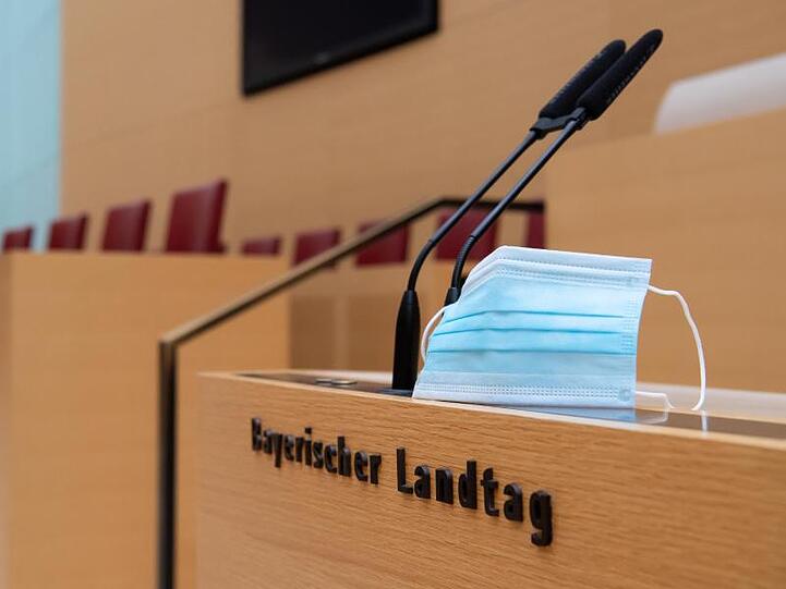 Ein Mund-Nase-Schutz befindet sich im Plenarsaal im bayerischen Landtag neben Mikrofonen. Foto: Sven Hoppe/dpa