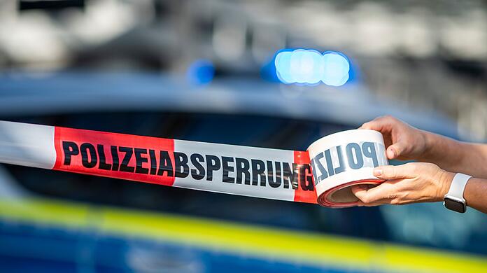 Ein Absperrband wird vor einem Polizeiwagen ausgerollt.
