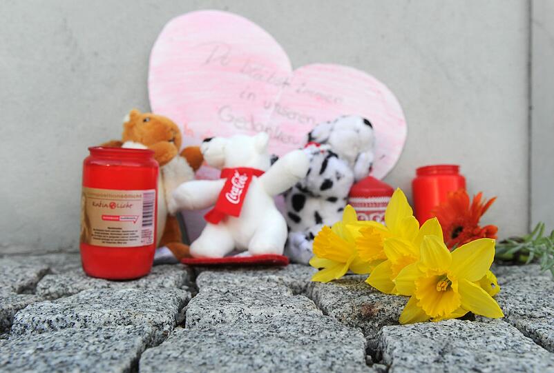 Blumen, Kerzen, Stofftiere und ein Papierherz mit der Aufschrift "Du bleibst immer in unseren Gedanken" liegen in Unterföhring vor einem Hauseingang an Gedenken an die 16-jährige Larissa.