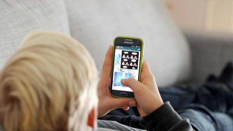 Ein Kind liegt auf einem Sofa und blickt auf sein Smartphone. Ein Kind liegt auf einem Sofa und blickt auf sein Smartphone.