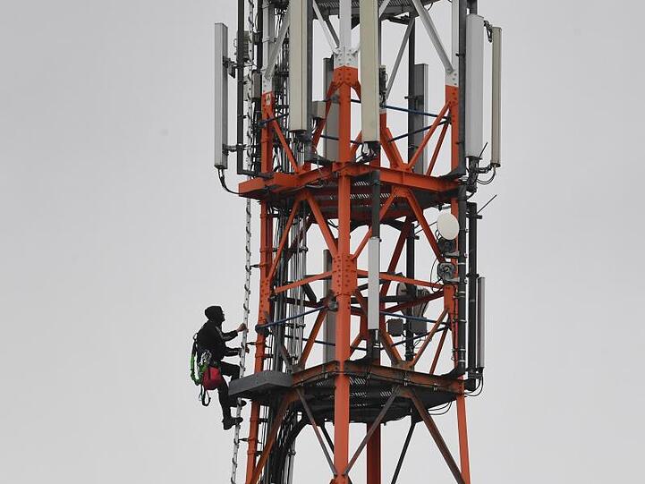 Ein Techniker klettert an einem Funkmast neben Mobilfunkantennen für den Mobilfunkstandard 5G.