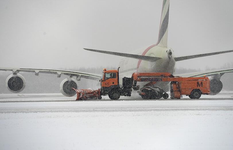 Ein Schneepflug fährt am 30.12.2014 auf dem Flughafen in München an einem parkenden Flugzeug vorbei. (Symbolbild)
