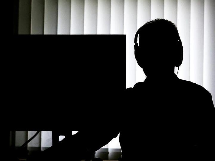 Ein Beamter sitzt für eine Telefonüberwachung mit Kopfhörern vor einem Computer. Foto: Christian Charisius/dpa/Archivbild