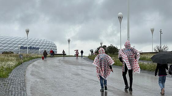Bergankunft im Regen. Ein paar Lyon-Fans kommen mit dem Regencape der Tour de France 2025 zur Allianz Arena.