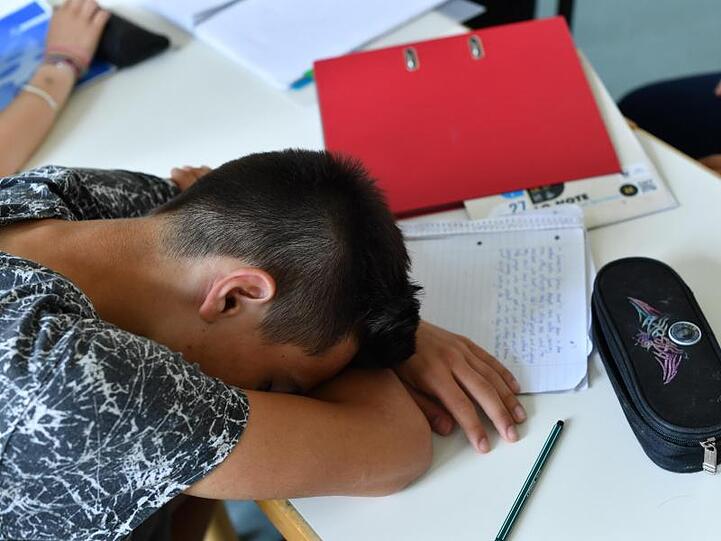 Ein Schüler hat seinen Kopf zwischen Schreibutensilien und Schulheften im Unterricht auf die Schulbank gelegt. Foto: Jens Kalaene/Archiv