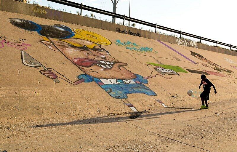 Die Kinder scheren sich nicht um diese etwas lächerlich wirkende Figur aus der Politik. Sie spielen auf der riesigen Graffiti-Karikatur an der Grenze zwischen Mexiko und den USA Fußball.