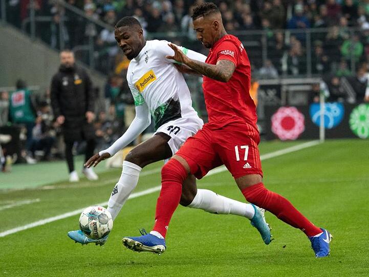 Gladbachs Marcus Thuram (l) und Bayerns Jerome Boateng versuchen den Ball zu spielen. Foto: Federico Gambarini/dpa