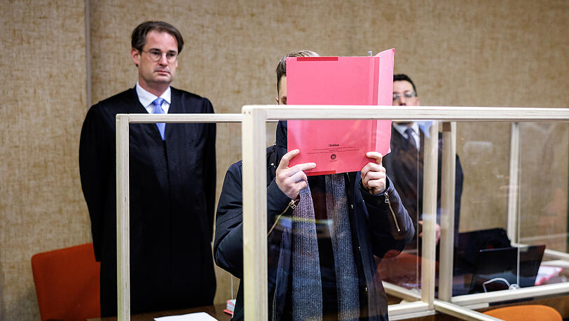 Der Angeklagte (M.) steht beim Prozessauftakt im Gerichtssaal.