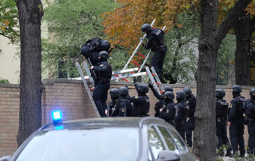 Polizisten mit Schutzhelmen übersteigen eine Mauer am jüdischen Friedhof.