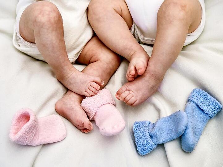 Rosa und blaue Söckchen für ein Mädchen und einen Jungen und die nackten Babybeine von Zwillingen. Foto: Patrick Pleul/dpa-Zentralbild/dpa/Archivbild