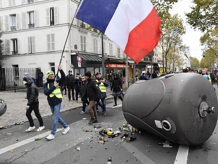 Ein Demonstrant der "Gelbwesten" hält in Paris die französische Fahne in die Luft, als er an einem umgestoßenen Altglascontainer vorbeigeht.