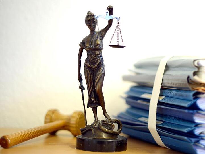 Die Justitia steht neben Akten und einem Holzhammer. Foto: Volker Hartmann/dpa/Archivbild