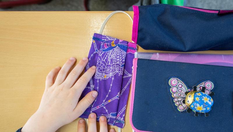 Eine Schülerin einer Grundschulklasse legt ihren Mundschutz neben ihre Schulmappe. Eine Schülerin einer Grundschulklasse legt ihren Mundschutz neben ihre Schulmappe.