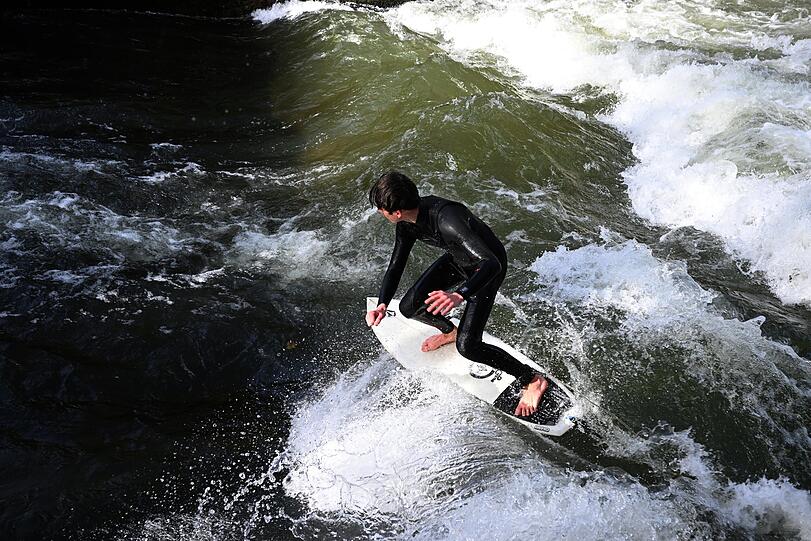 Ein Surfer fährt bei Sommerwetter in der Landeshauptstadt München auf der Eisbachwelle.