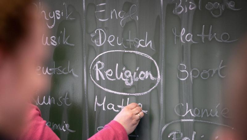 Eine Lehrerin schreibt mit Kreide einen Stundenplan mit Religionsunterricht an eine Tafel. Foto: Friso Gentsch/Archivbild Eine Lehrerin schreibt mit Kreide einen Stundenplan mit Religionsunterricht an eine Tafel. Foto: Friso Gentsch/Archivbild