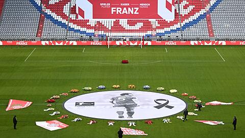 Fahnen von FCB-Fanclubs liegen neben einem überlebensgroßen Beckenbauer-Bild im Mittelkreis der Allianz Arena.