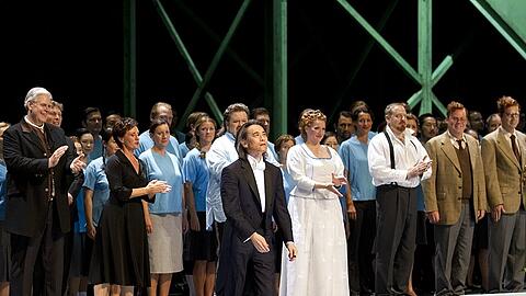Geschafft! Erleichtert tritt Dirigent Kent Nagano nach Wagners &bdquo;Lohengrin&ldquo; vor seine Mannschaft. Hinter ihm sieht man das hohe Paar, Emily Magee (Elsa) im weißen Hochzeitsdirndl und Johan Botha (Lohengrin) im legeren Hemd. Ganz links applaudieren Kristinn Sigmundsson (Heinrich) und die als Ortrud stürmisch gefeierte Waltraud Meier.