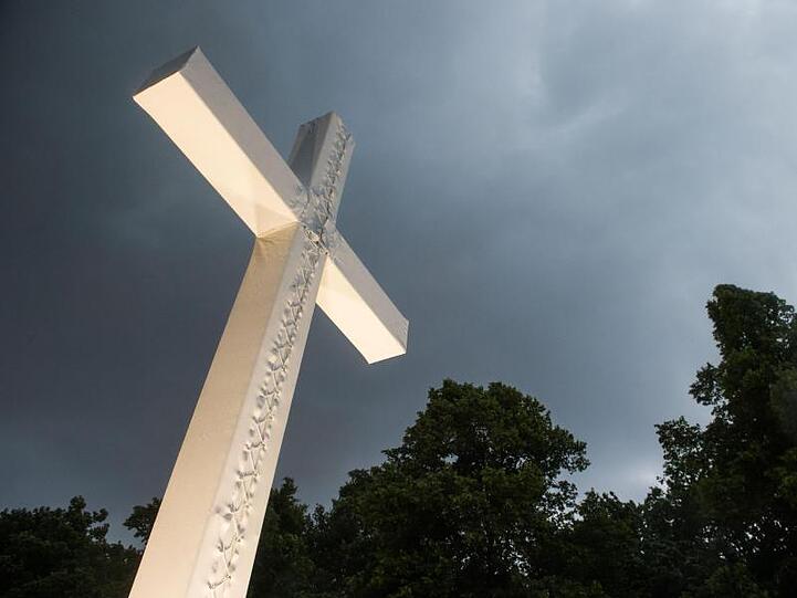 Dunkle Wolken ziehen über ein üYberdimensioniertes Kreuz auf. Foto: Lino Mirgeler/dpa/Archivbild