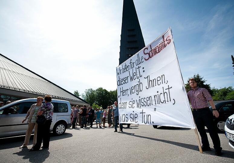 Protestplakat vor der Kirche gegen den Passauer Bischof: &bdquo;Wir beten für alle Schramls dieser Welt: Herr, vergib ihnen, denn sie wissen nicht, was sie tun.