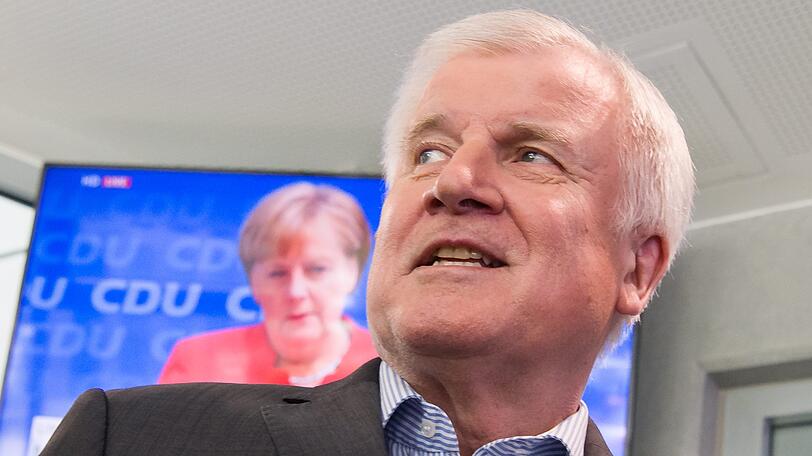 Horst Seehofer, CSU-Vorsitzender und Bundesminister für Inneres, Heimat und Bau, geht auf seinem Weg zu einer Pressekonferenz im Anschluss CSU-Vorstandssitzung an einem Fernseher vorbei, auf dem die Pressekonferenz von Bundeskanzlerin Angela Merkel übertragen wird.