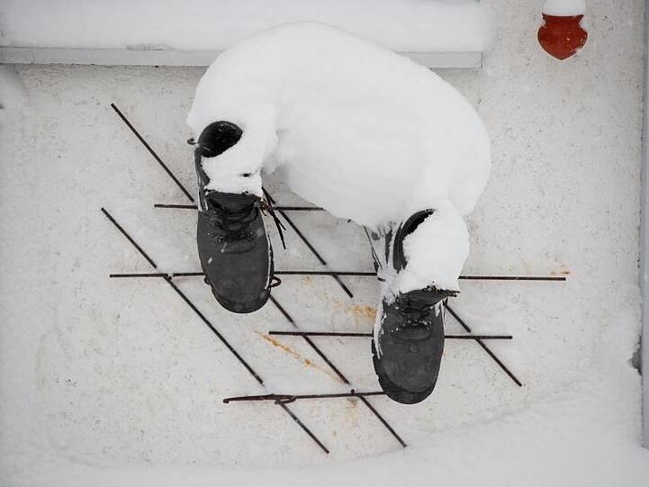 Schuhe hängen an einer verschneiten Hausmauer. Foto: Erwin Scheriau