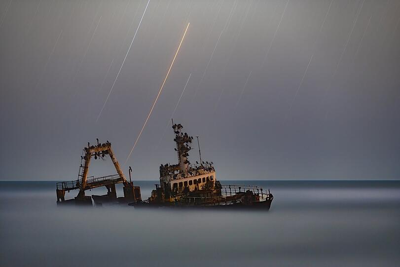 "People and Space"-Gewinner: Dieses Foto von Vikas Chander ist an der Atlantik-Küste Namibias entstanden. Das Schiff Zeila ist dort 2008 gestrandet. Dahinter sind Sterne in verschiedenen Farben zu sehen. Belichtungszeit: 30 Minuten.