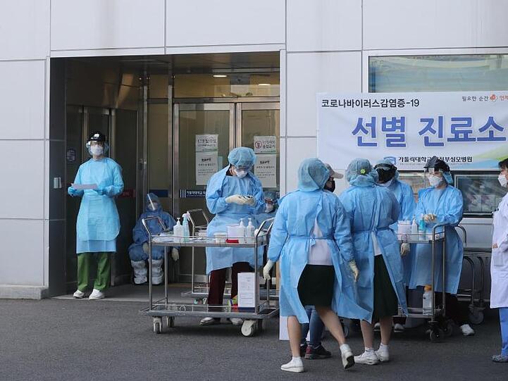 Medizinisches Personal in Schutzausrüstung steht vor einem Krankenhaus in Südkorea.