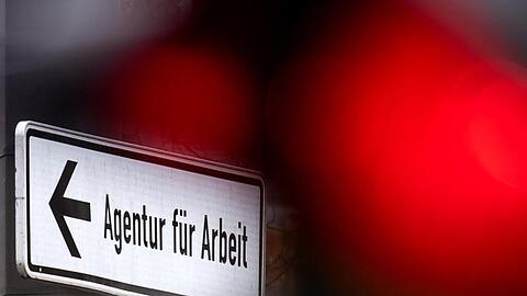 Eine rote Ampel leuchtet vor einem Schild, das auf die Agentur für Arbeit hinweist. Foto: Sina Schuldt/dpa/Symbolbild