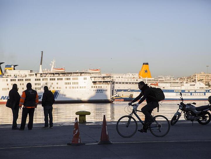 Passanten stehen vor den angedockten Fähren im Hafen von Piräus.