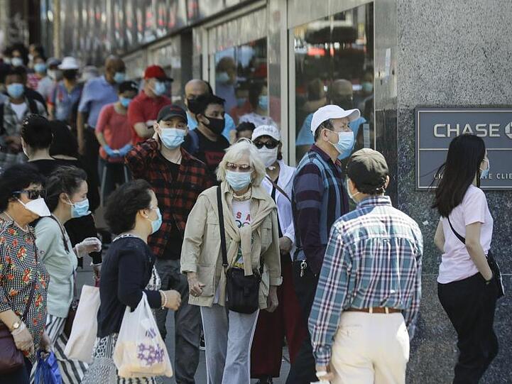 Menschen mit Masken warten im New Yorker Stadtbezirk Queens vor dem Eingang einer Bank.