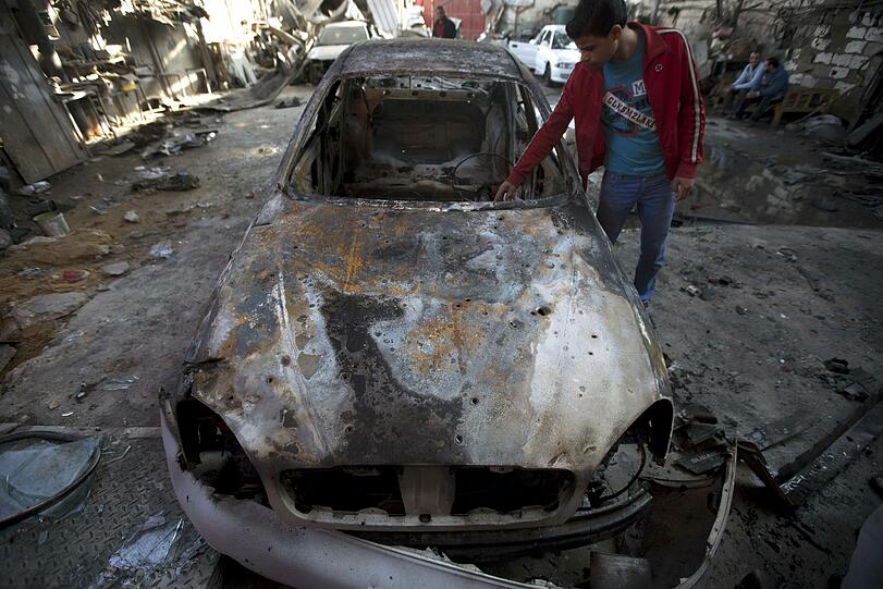 Ein junger Palästinenser begutachtet in Jabalia (im nördlichen Gazastreifen) ein ausgebranntes Auto, das bei einem nächtlichen Luftangriff des israelischen Militärs in Mitleidenschaft gezogen wurde.