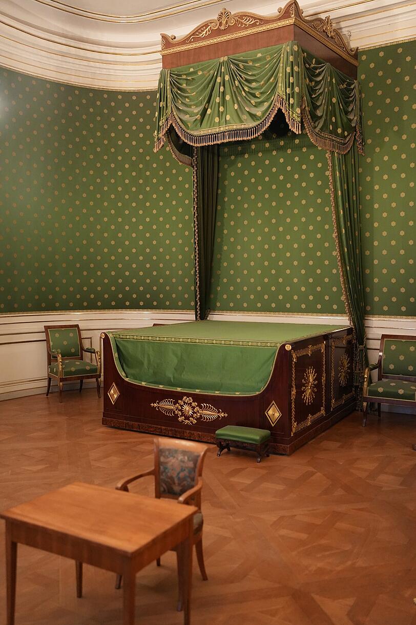Der Blick auf das königliche Bett mit Schemel, davor stehen ein kleiner Tisch und ein Stuhl für Kinder. Der Blick auf das königliche Bett mit Schemel, davor stehen ein kleiner Tisch und ein Stuhl für Kinder.