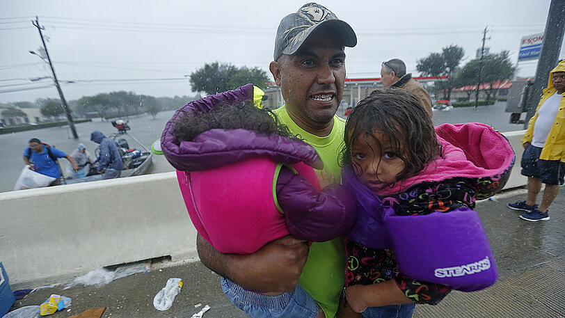 Ein Mann trägt in Houston Kinder, nachdem sie von Feuerwehrleuten aus dem in der Folge des Tropensturms Harvey überfluteten Gebiet gerettet worden waren.