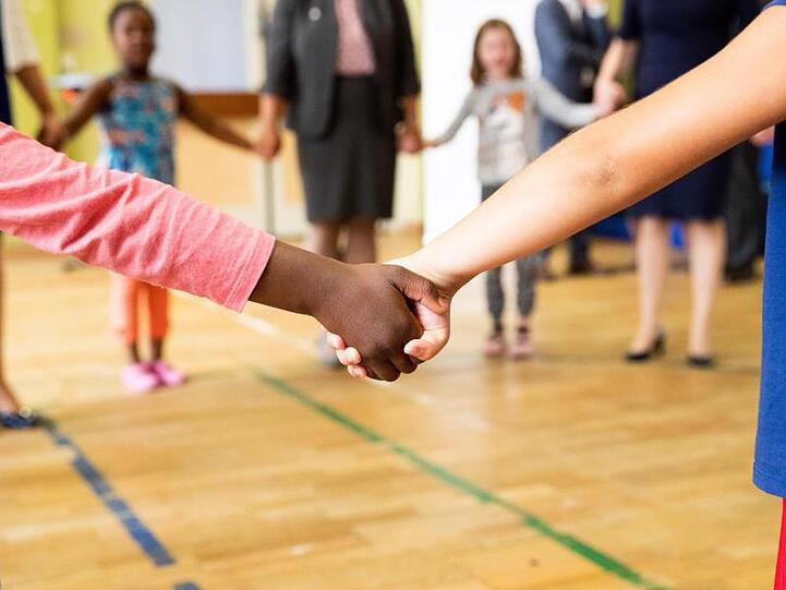 Hand in Hand tanzen Kinder und Erzieherinnen in der Turnhalle einer Kita. Foto: Christian Charisius/dpa