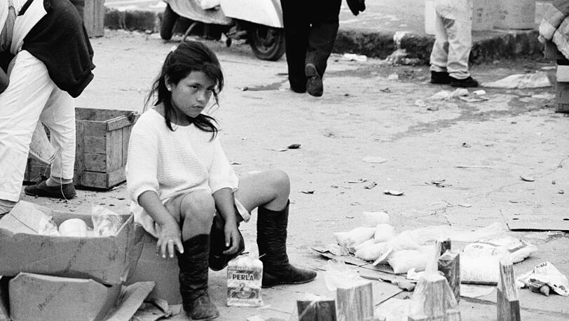 Olaf Unverzart hat das kleine Mädchen 1993 auf einem Straßenmarkt im ecuadorianischen Otovallo entdeckt. Was der ernste Blick erzählt? Und was das Mädchen außer den Packerln auf dem Boden sonst noch anbietet? Olaf Unverzart hat das kleine Mädchen 1993 auf einem Straßenmarkt im ecuadorianischen Otovallo entdeckt. Was der ernste Blick erzählt? Und was das Mädchen außer den Packerln auf dem Boden sonst noch anbietet?