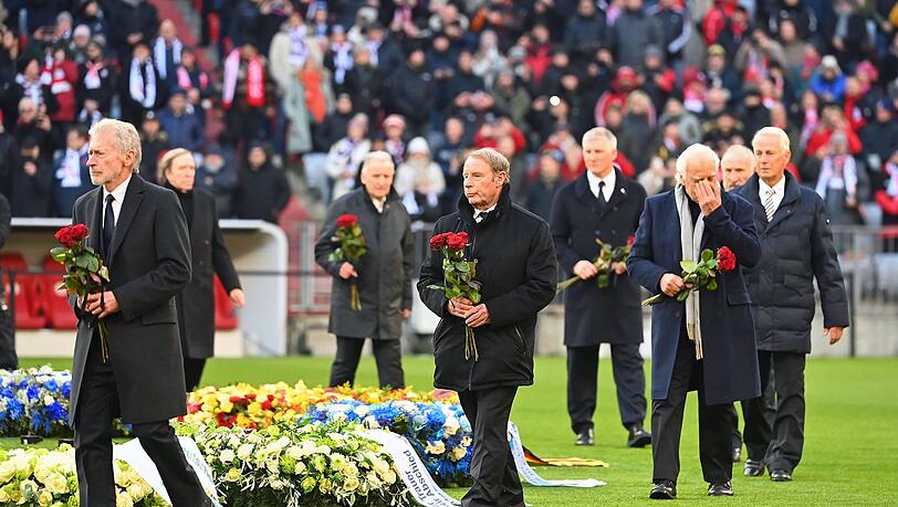 Elf Wegbegleiter Beckenbauers legen um den Mittelkreis Rosen nieder.